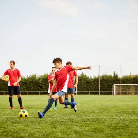 Full length of boy kicking ball on ground during training. Children are practicing soccer on field. They are in sports uniforms.